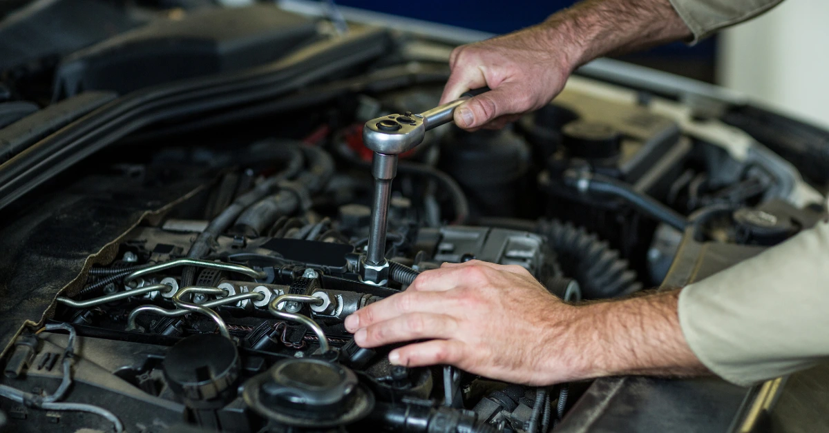 Auto mechanic working on an open engine bay with a ratchet wrench, a look at the hands-on effort behind every car servicing cost