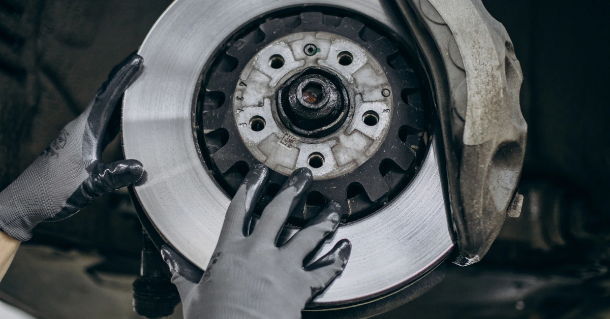 Mechanic in grey gloves handling a vehicle's clutch disc assembly underside, a clear example of the hands-on work behind clutch replacement cost.